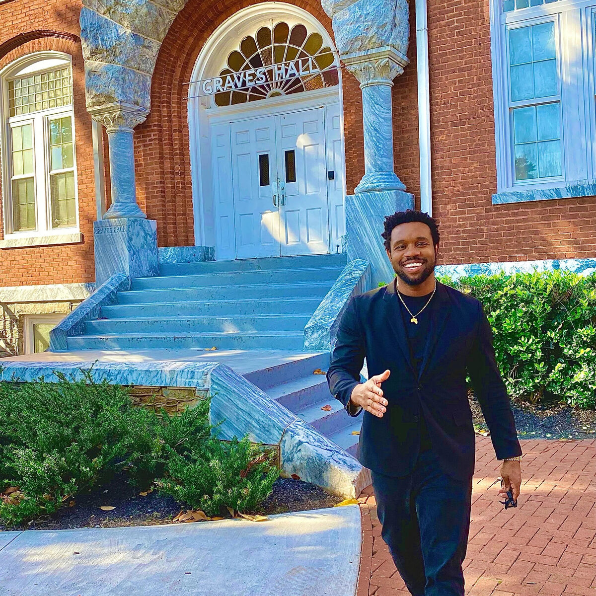 Bakari Akil extending a handshake in front of Graves Hall